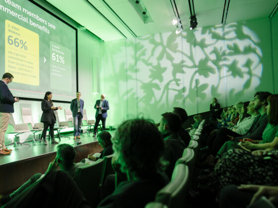 Four people standing on stage at Planet Peach presenting to an audience on commercial benefits.